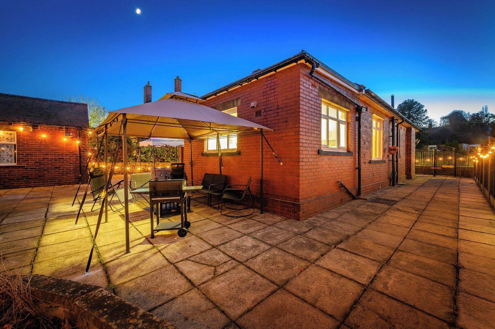 A brick house with a patio area, a barbecue grill, outdoor seating, and string lights.