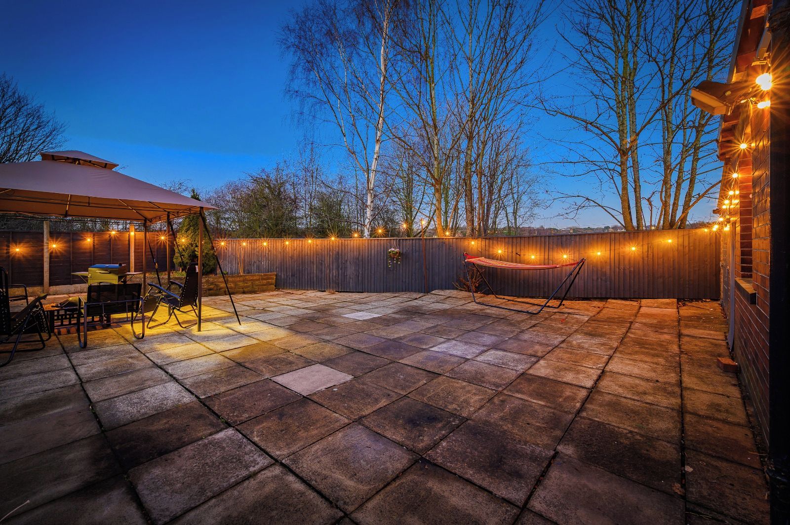 A patio area with a covered seating area, a hammock, and string lights.