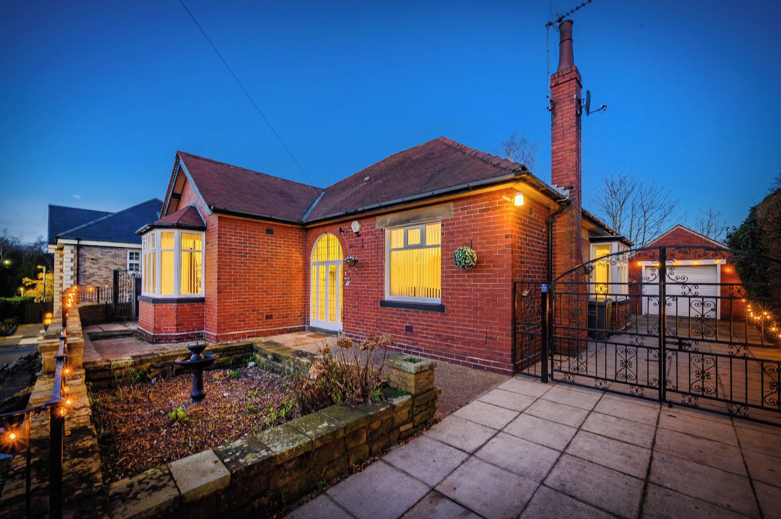 A brick house with a red roof, a chimney, and a gated driveway.