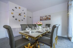 Comedor con mesa de mármol, sillas tapizadas en gris, un reloj de pared y un cuadro con motivos florales.