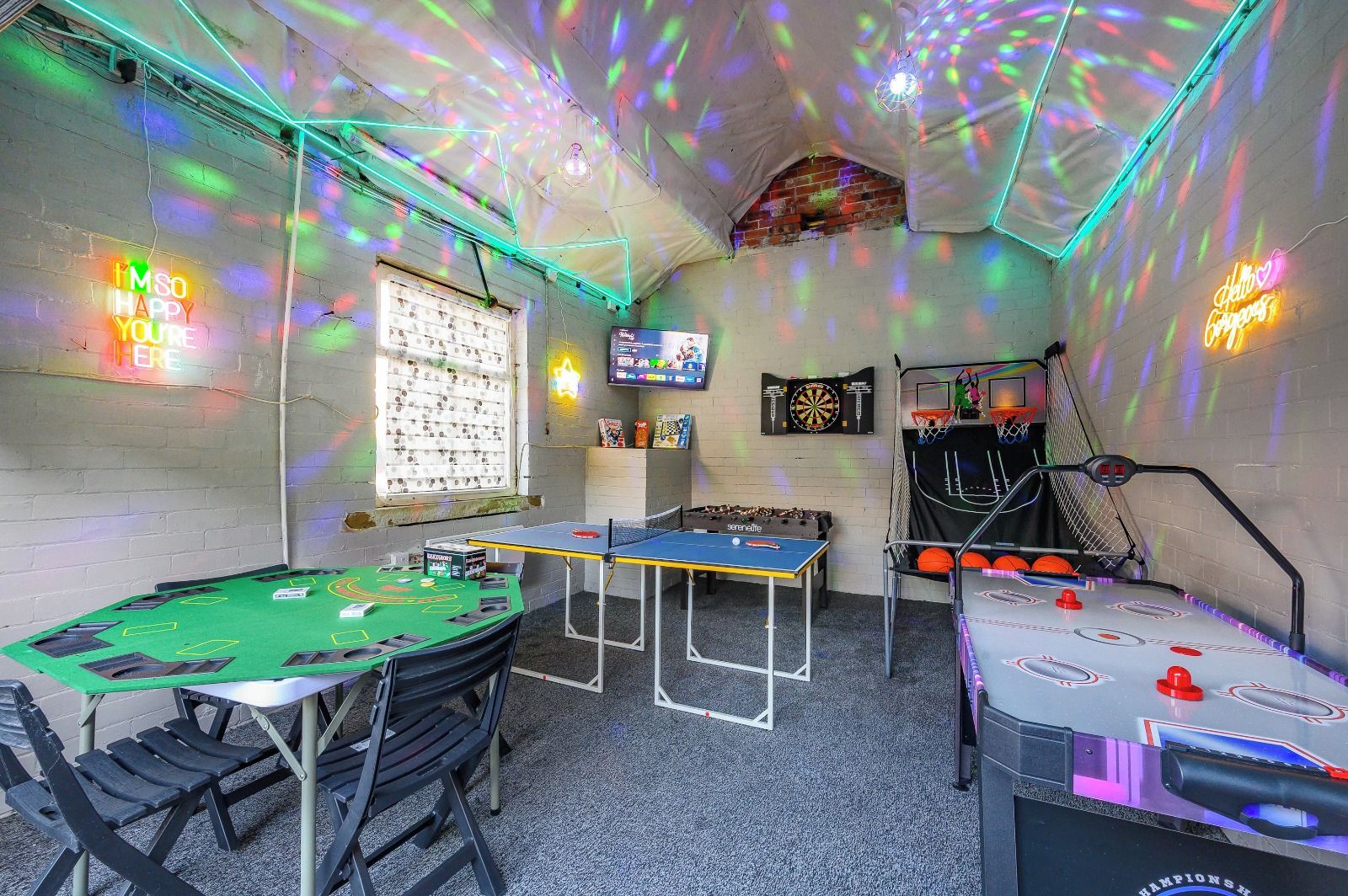 A room with a pool table, foosball table, dartboard, and a television.