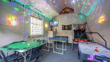 A room with a pool table, foosball table, dartboard, and a television.