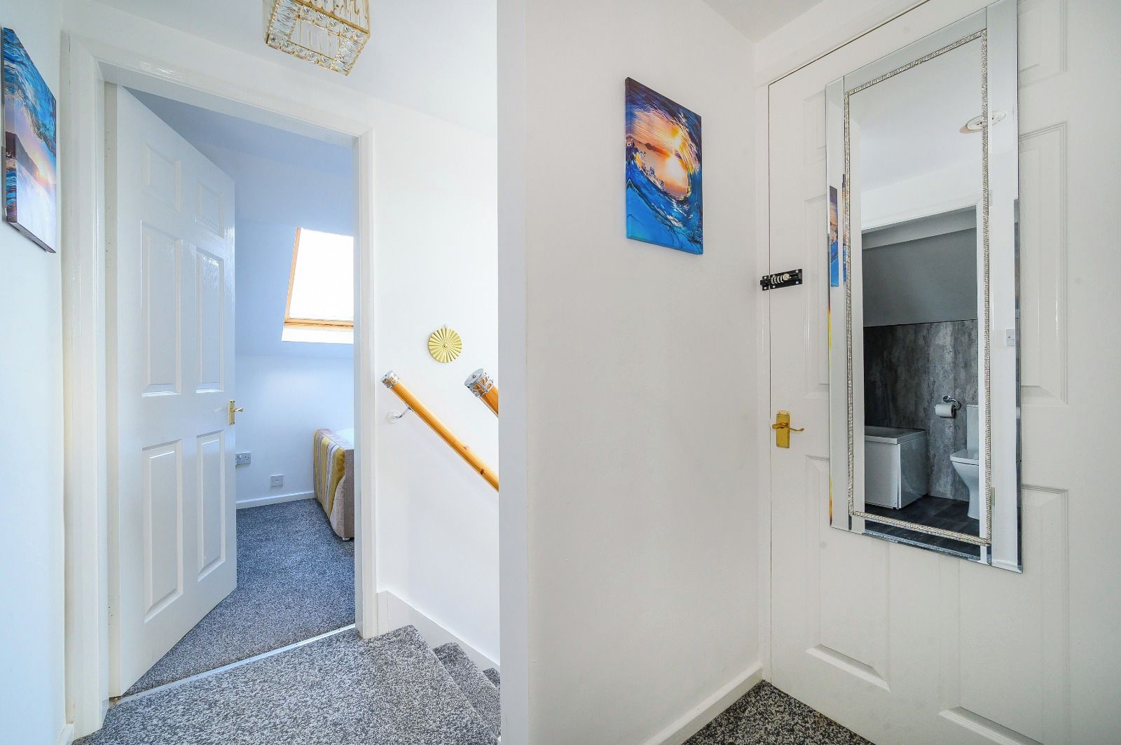 Een gang met een deur naar een badkamer, een klein raam en een aan de muur hangend schilderij.