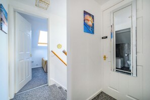 Un pasillo con una puerta que da a un baño, una ventana pequeña y un cuadro colgado en la pared.