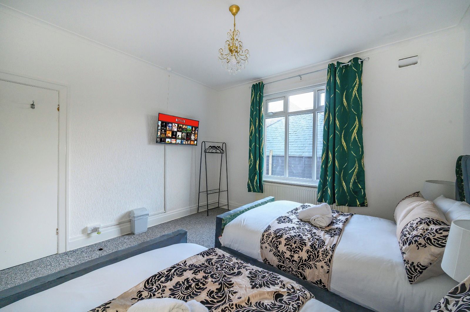 A hotel room with two beds, a TV mounted on the wall, a window with curtains, and a radiator.