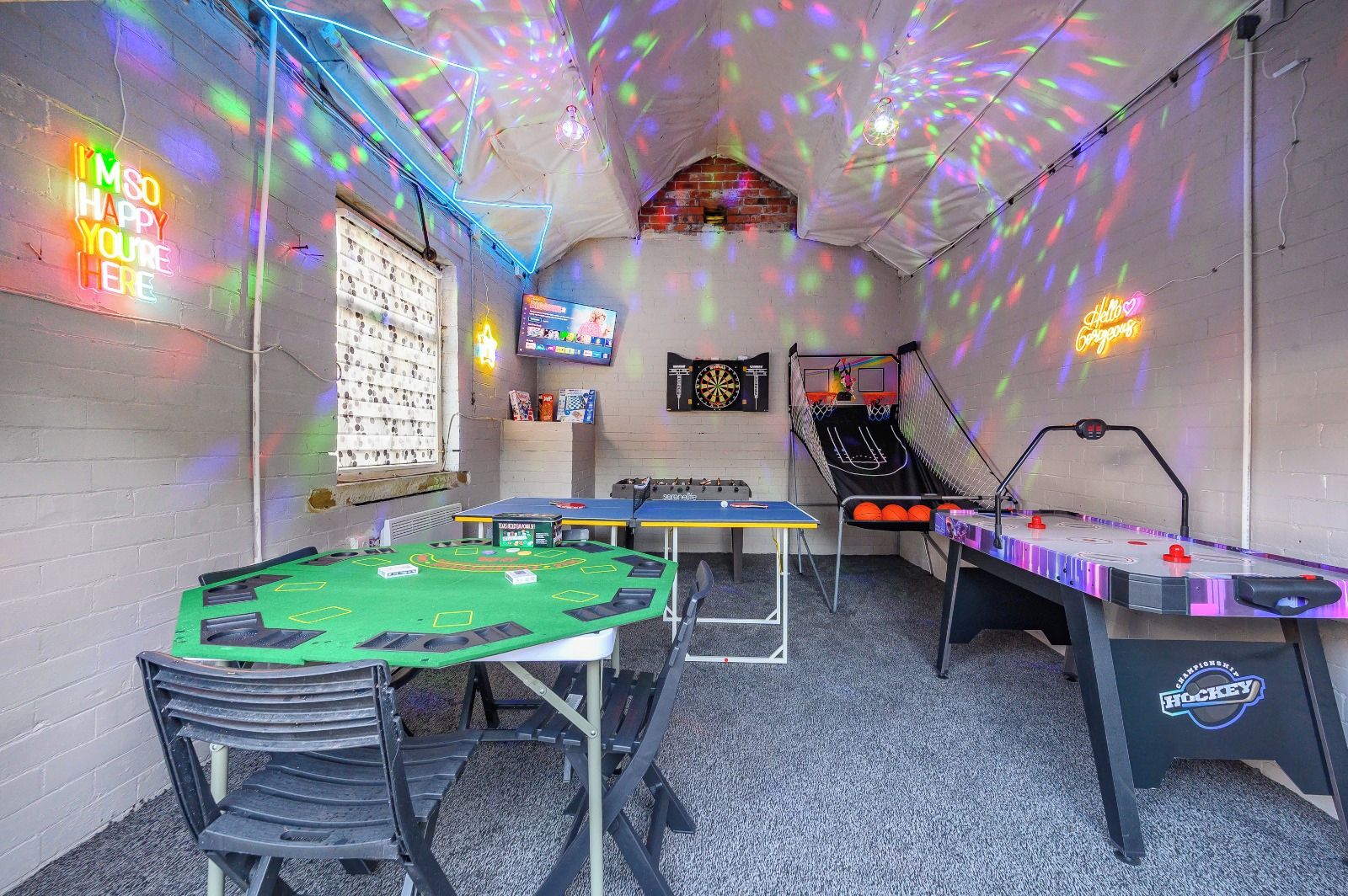 A room with a dartboard, a dartboard, a table tennis table, and a foosball table.