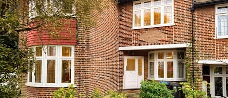 Une maison à deux étages, construite en briques, avec un toit rouge, des fenêtres à cadre blanc et une porte bien visible.