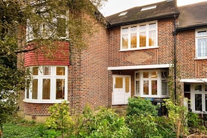 A two-story brick house with a red roof, white-framed windows, and a visible door. - Period 2-Bed Home · Sleeps 4 · Parking · Walk to Wimbledon Station (Greater London)