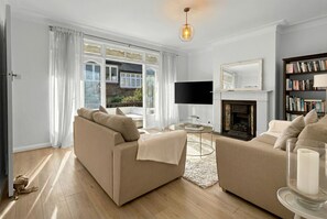 A living room with two sofas, a fireplace, a bookshelf, and a large window with curtains.