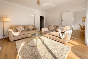 A modern living room with a beige sofa set, a glass coffee table, and a fluffy rug. - Period 2-Bed Home · Sleeps 4 · Parking · Walk to Wimbledon Station (Greater London)