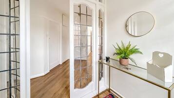 A hallway with a glass door, a mirror on the wall, a small potted plant, and a glass table with a white object on it.