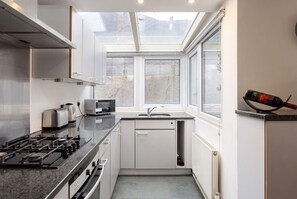 A compact kitchen with a gas stove, toaster, and a window above the sink. - 3-Bed Flat · Sleeps 6 · Workspace · 10-Min Walk to Wimbledon Station (Greater London)