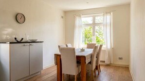 Un comedor con una mesa y sillas, un reloj en la pared y una ventana con cortinas.