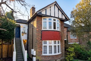 A two-story house with a red front, a white window, and a staircase leading to the door. - 3-Bed Flat · Sleeps 6 · Workspace · 10-Min Walk to Wimbledon Station (Greater London)