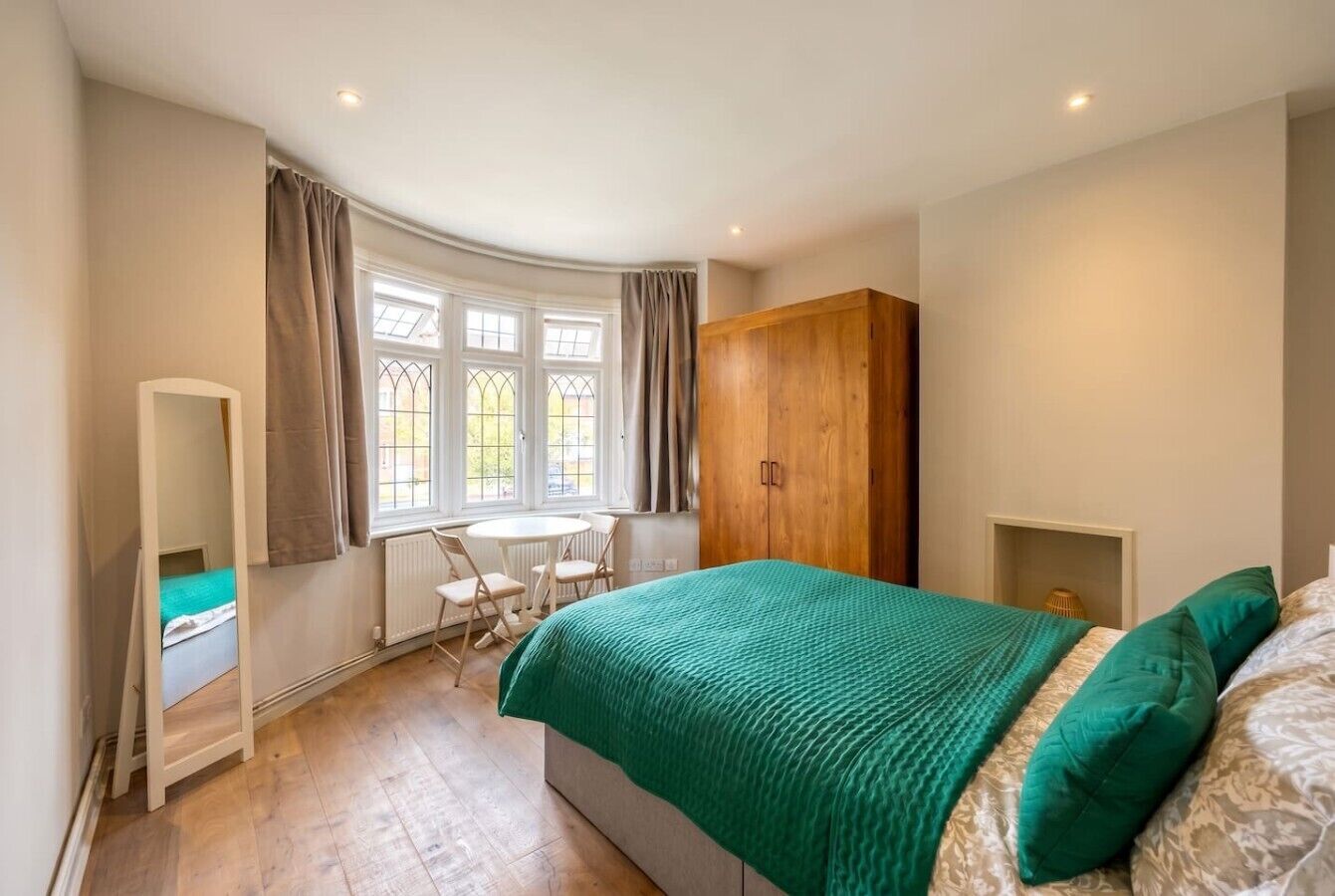 A bedroom with a bed, a wooden wardrobe, a desk with a chair, and a window with curtains.