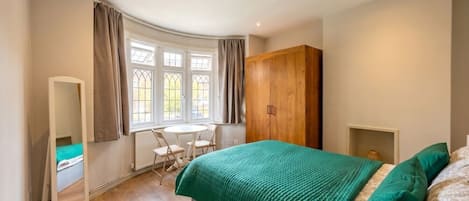 Un dormitorio con cama, armario de madera, escritorio con silla y ventana con cortinas.