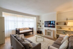 A living room with a sofa set, a coffee table, a fireplace, and a television mounted on the wall. - 3-Bed Flat · Sleeps 6 · Workspace · 10-Min Walk to Wimbledon Station (Greater London)