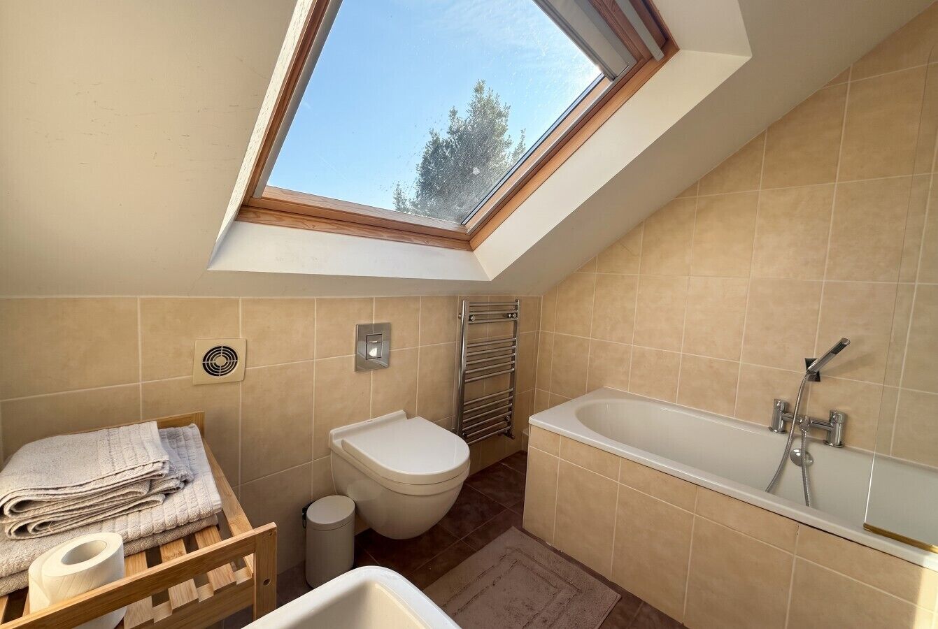 Une salle de bain moderne dotée d’une lucarne, de toilettes, d’une baignoire et d’un porte-serviettes.