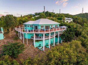 Een turquoise huis met twee verdiepingen en een balkon, omringd door weelderige begroeiing.