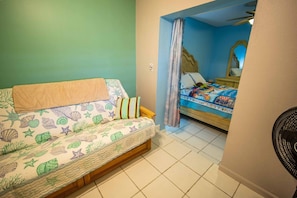 Een kamer met een bed, een slaapbank en een ventilator.