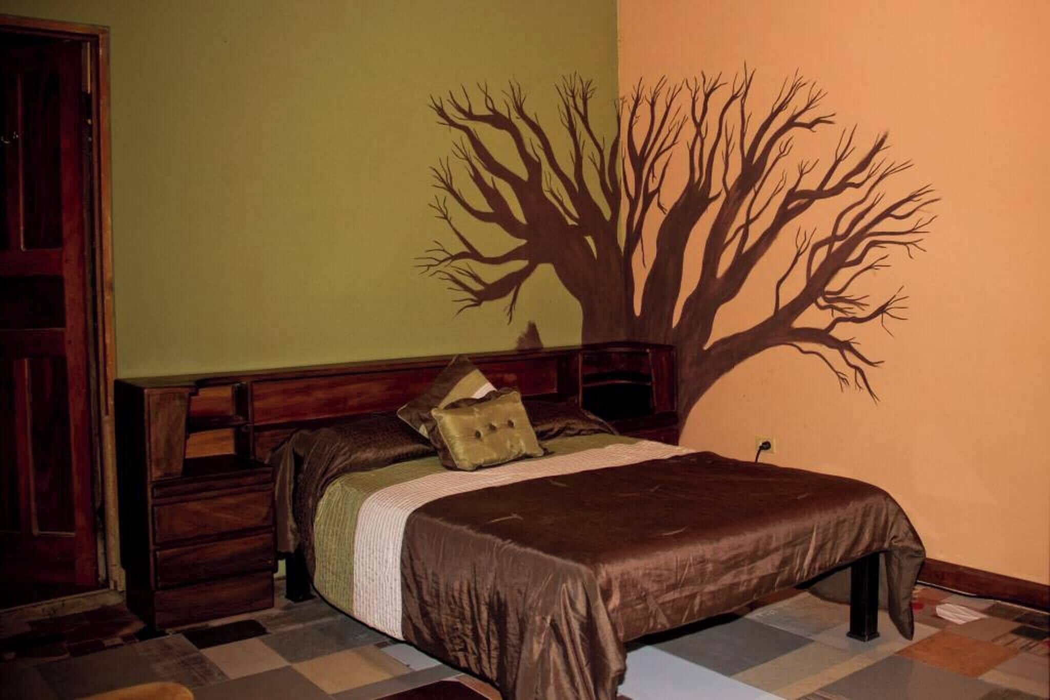 A bedroom with a bed, a dresser, a nightstand, and a wall mural of a tree.