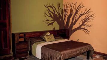 A bedroom with a bed, a dresser, a nightstand, and a wall mural of a tree.