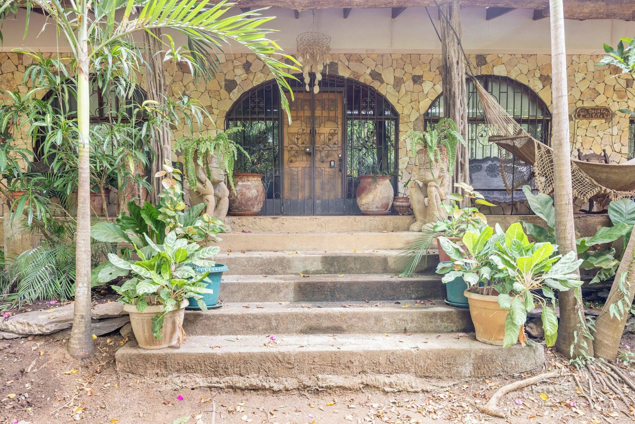Un bâtiment en pierre avec une porte en bois, des plantes en pot et un hamac.