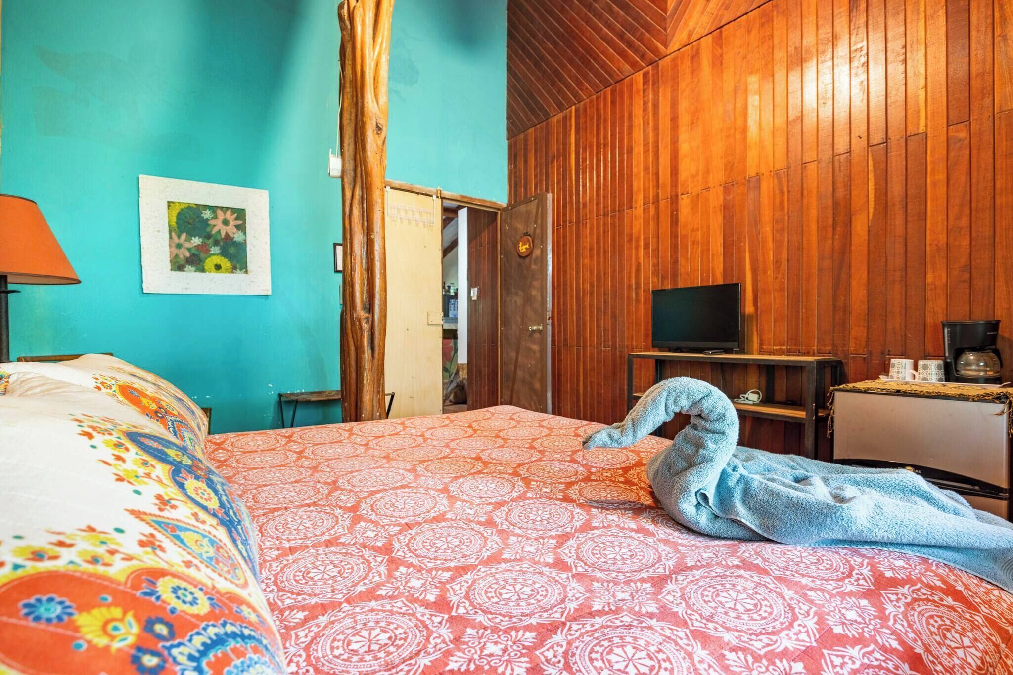 A hotel room with a bed, a television, a coffee maker, and a door leading to a bathroom.