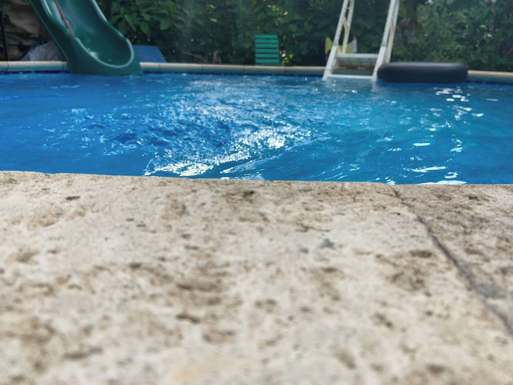A swimming pool with a slide and a green fence in the background.