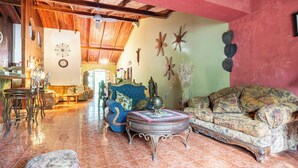 Un salón amplio con techo alto, un sofá azul, un sillón estampado y una pared decorativa con motivos de estrellas de mar y flores.