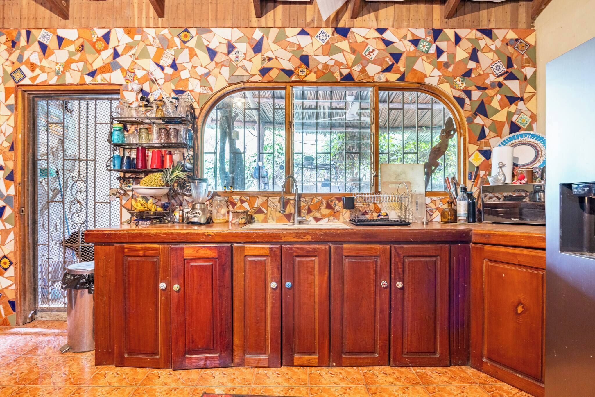 A kitchen with wooden cabinets, a large window, and a tiled backsplash.