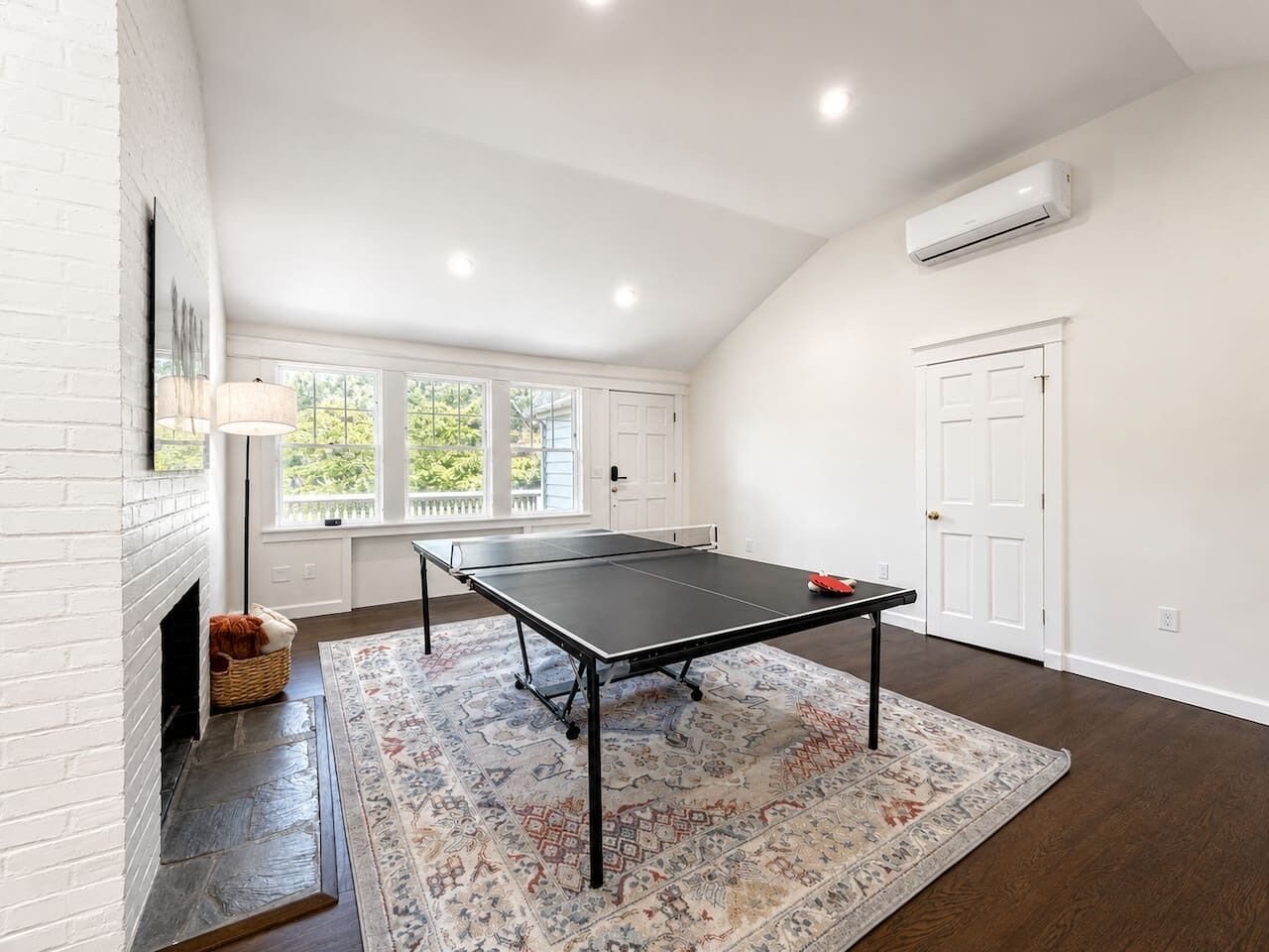 A room with a ping pong table, a fireplace, and a large window.
