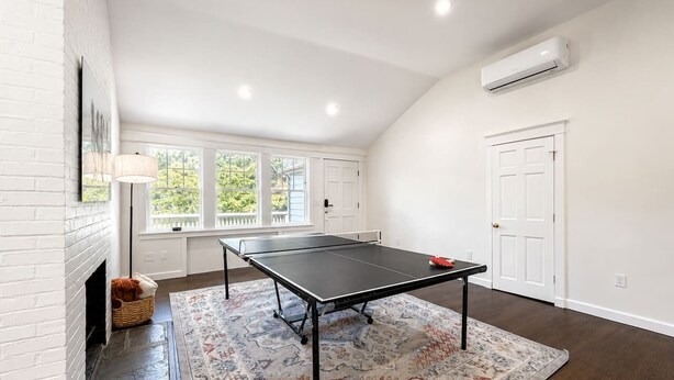 Et værelse med et ping pong bord, pejs og et stort vindue.
