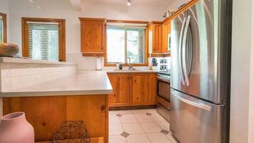A kitchen with wooden cabinets, a stainless steel refrigerator, and a window with blinds.