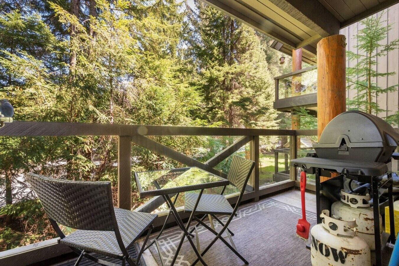 A covered outdoor area with a grill, chairs, and a view of trees.