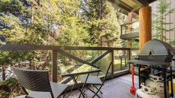 A covered outdoor area with a grill, chairs, and a view of trees.
