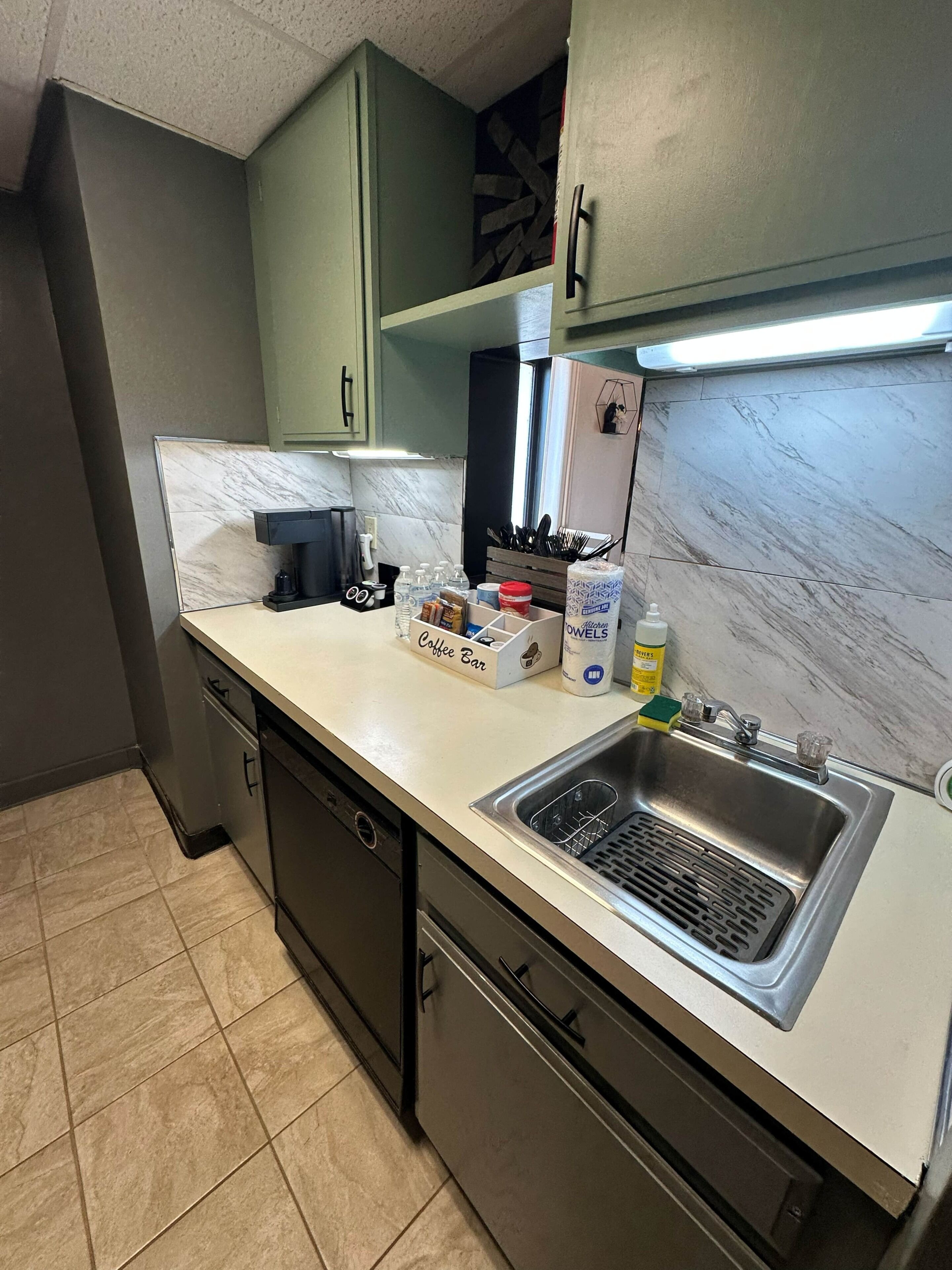 A kitchen with a stainless steel sink, a coffee bar, and a dish rack.