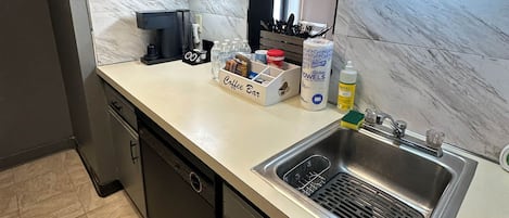 A kitchen with a stainless steel sink, a coffee bar, and a dish rack.