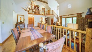 A spacious dining area with a long wooden table, surrounded by chairs with woven seats. A wooden railing separates the dining area from a lower level. - Adirondacks 6 | Fireplace, Restaurant, Pool, Spa (Blowing Rock)
