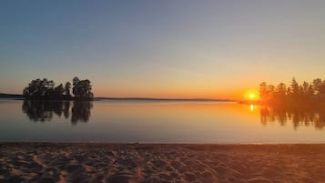 Ein ruhiger See mit Sonnenuntergang, Bäumen und einem Sandstrand.