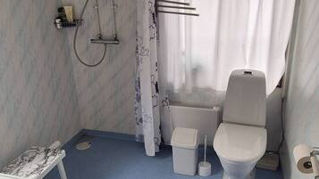 Un baño pequeño con lavamanos, inodoro y zona de ducha blancos.