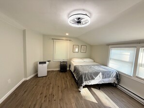 A bedroom with a bed, a ceiling fan, a heater, a window with blinds, and a radiator.