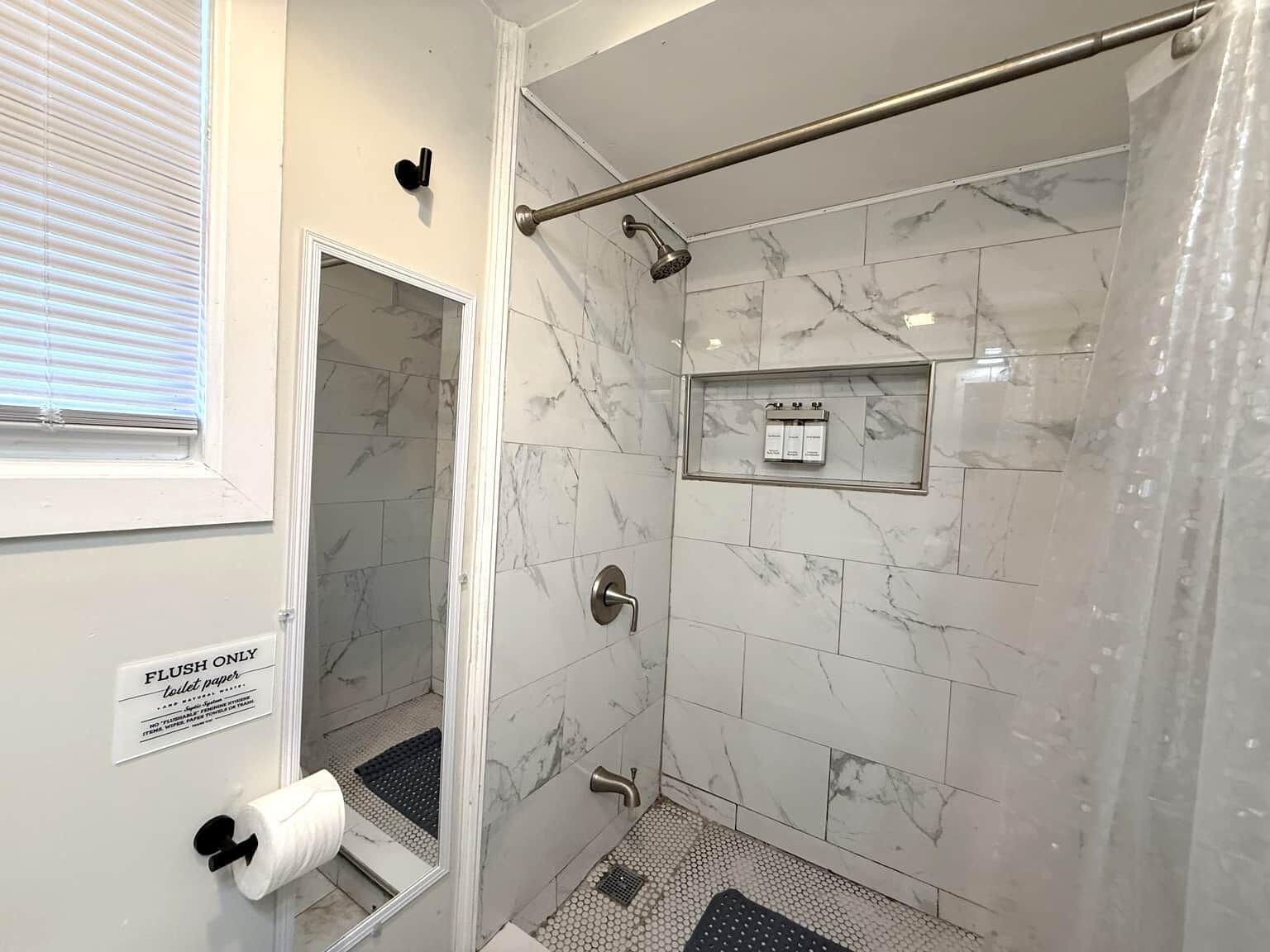 A bathroom with a shower, toilet paper, and a sign indicating flush-only use.