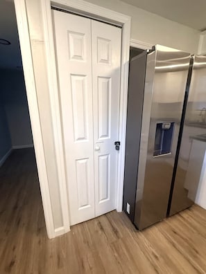A kitchen with a stainless steel refrigerator, a white double door, and wooden flooring.