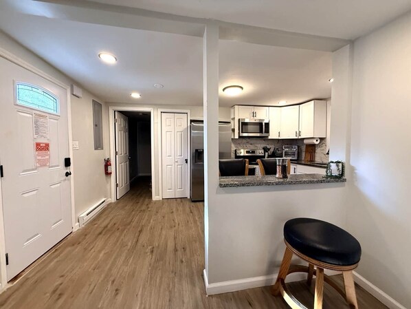 A modern kitchen with white cabinets, stainless steel appliances, and a wooden stool.