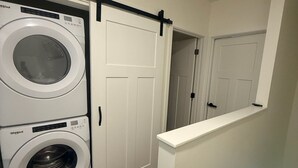 Pesuhuoneessa on kaksi päällekkäin asennettua Whirlpool-merkkiä pyykinpesukone ja -kuivausrumpu, liukuva latoon tyylinen ovi ja valkoinen ovi, joka johtaa toiseen huoneeseen.