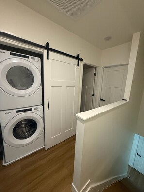 Ein Waschraum mit zwei übereinander gestapelten Whirlpool Waschmaschinen und Trocknern, einer Schiebetür im Scheunenstil und einer weißen Tür, die in einen anderen Raum führt.