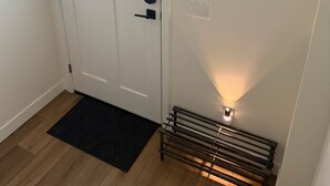 Valkoinen ovi, jossa on ikkuna, musta ovimatto, seinälle kiinnitetty peili ja patteri.