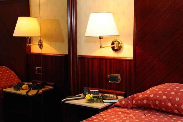 A hotel room with a bed, two bedside tables, a lamp, a telephone, and a small decorative item on the nightstand.
