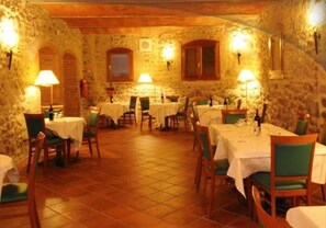A restaurant with stone walls, round tables, and green chairs.
